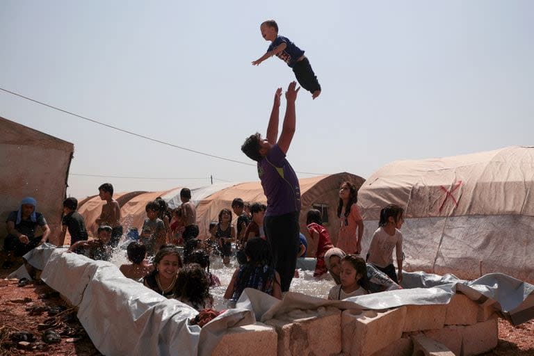 Un grupo de niños es supervisado por algunos adultos en una piscina improvisada en medio de las altas temperaturas en un campamento para desplazados internos en Zardana, en la provincia de Idlib, en el noroeste de Siria