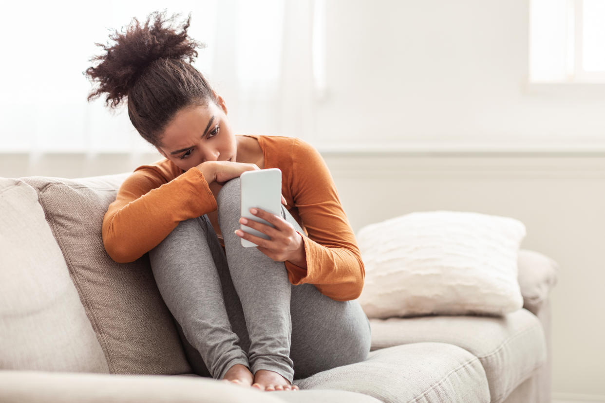 Young woman sitting at home on sofa with phone. (Getty Images)