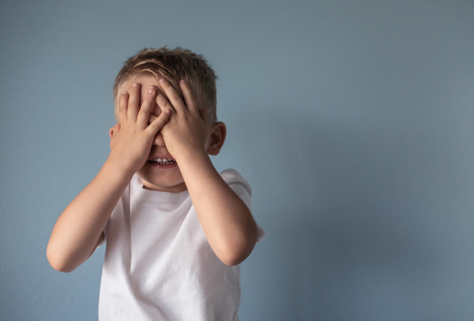 Little boy covering his eyes against gray background.