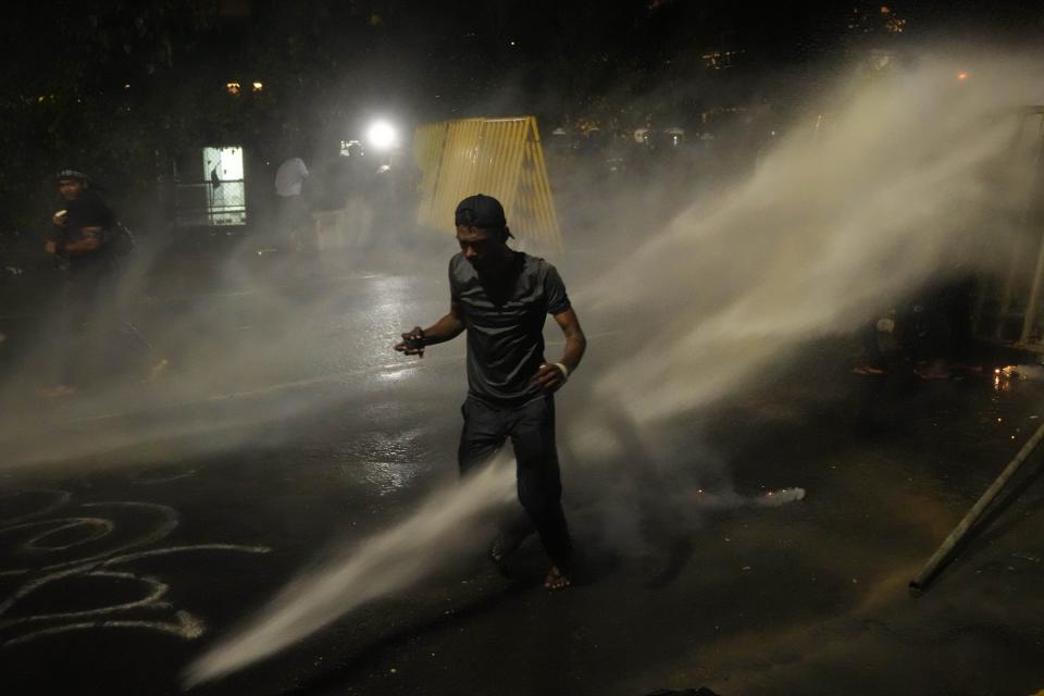 A protester runs for cover as police fire tear gas shells near the president's official residence in Colombo, Sri Lanka, Saturday, May 28, 2022. Police fired tear gas and water canon on protesters who marched toward the president Gotabaya Rajapaksa's barricaded residence demanding his resignation. (AP Photo/Eranga Jayawardena)