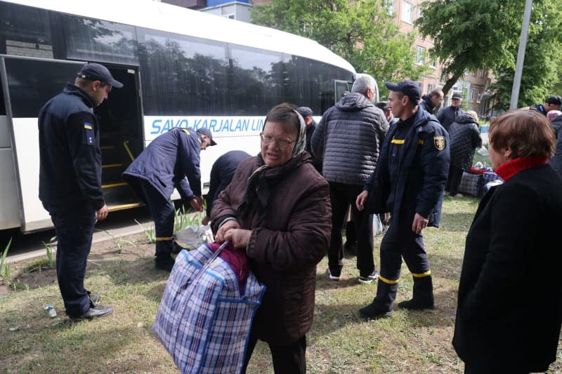 An elderly woman carries a bag next to a bus parked at a center for people brought to safety from the Kharkiv region. -/Ukrinform/dpa