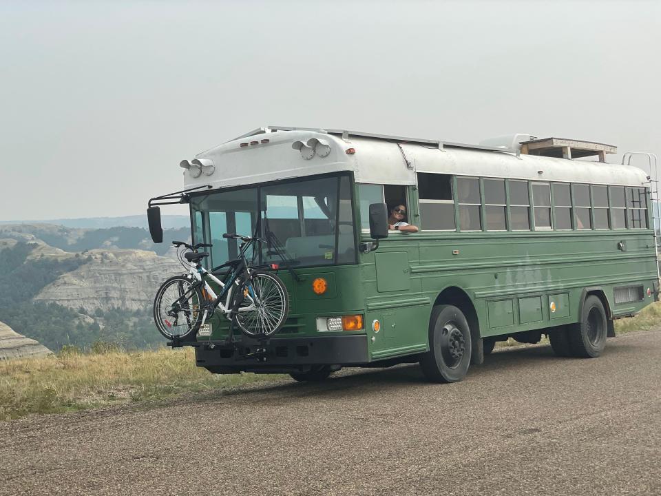A green bus on a gravel road with mountain range in the background