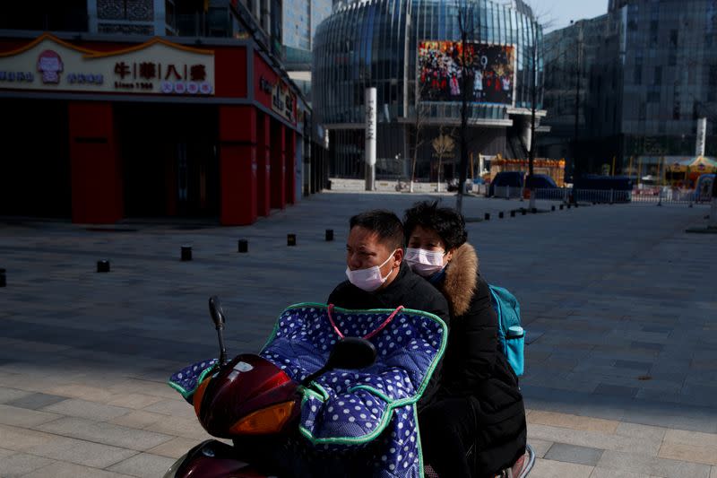 People wearing face masks ride a scooter through a deserted shopping area in Changsha