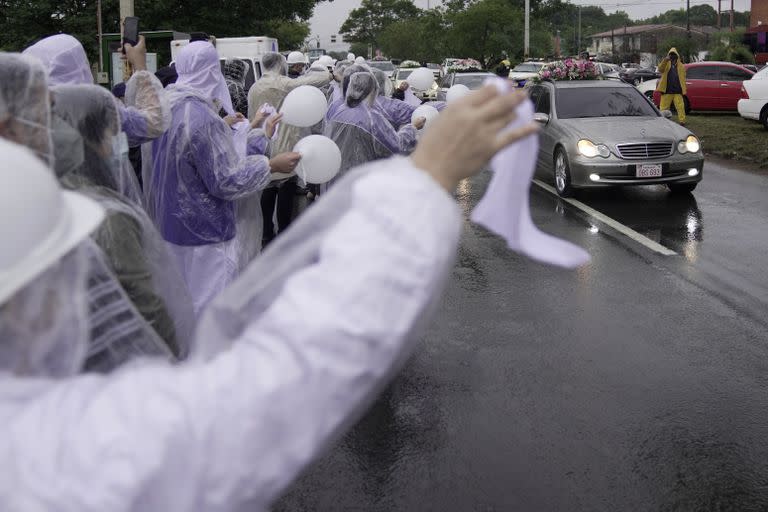 Personas que trabajaron para Luis Pettengill observan los coches fúnebres que transportan los restos de su difunto jefe, su esposa Sophia López Moreira, hermana de la primera dama de Paraguay, y sus tres hijos, luego de que sus restos llegaran a Asunción, Paraguay