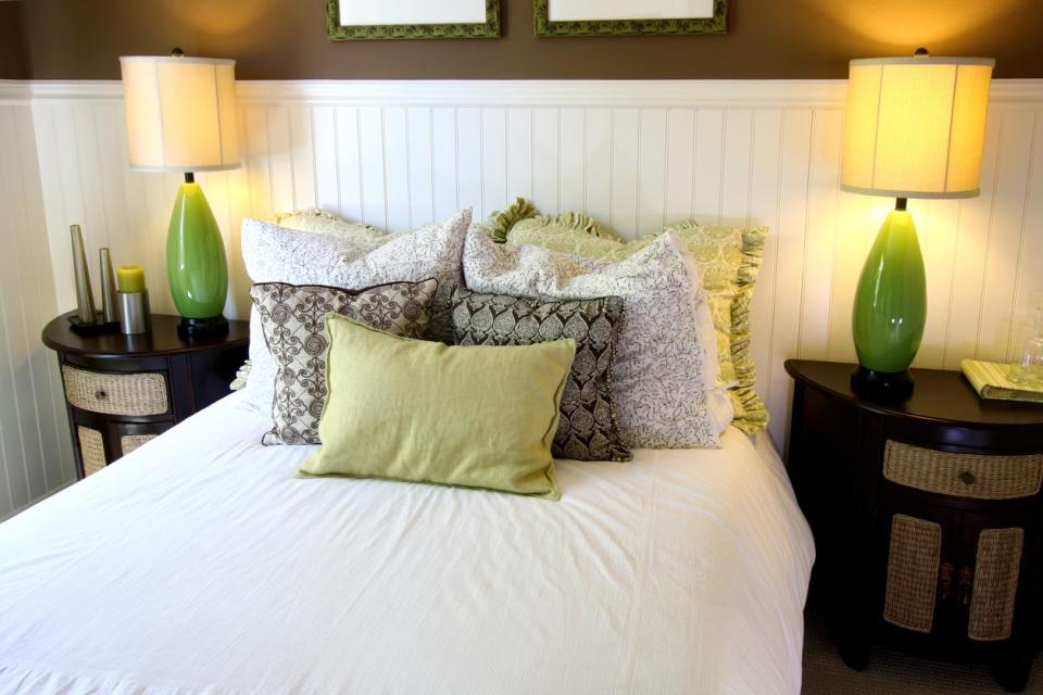 A beautifully decorated bedroom, with lots fluffy pillows on the bed and a beadboard wall behind it.