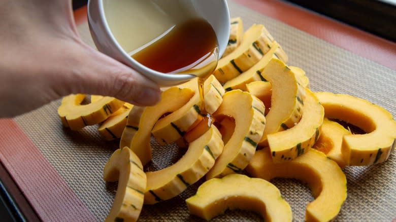 Hand pouring maple syrup on delicata squash slices