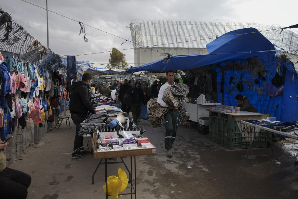 A vendor sells goods to Palestinian laborers as they cross from Israel back to the West Bank at the end of working day, next to a section of Israel's separation barrier in Meitar crossing in the West Bank, March 10, 2022. For more than two years, the Biden administration has said that Palestinians are entitled to the same measure of “freedom, security and prosperity” enjoyed by Israelis. Instead, they've gotten U.S. aid and permits to work inside Israel and its Jewish settlements. The inconsistency is likely to come up when President Joe Biden visits Israel and the occupied West Bank this week for the first time since assuming office. (AP Photo/Mahmoud Illean)