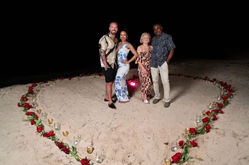 Family of four stood on a beach and surrounded by roses arranged in a heart shape