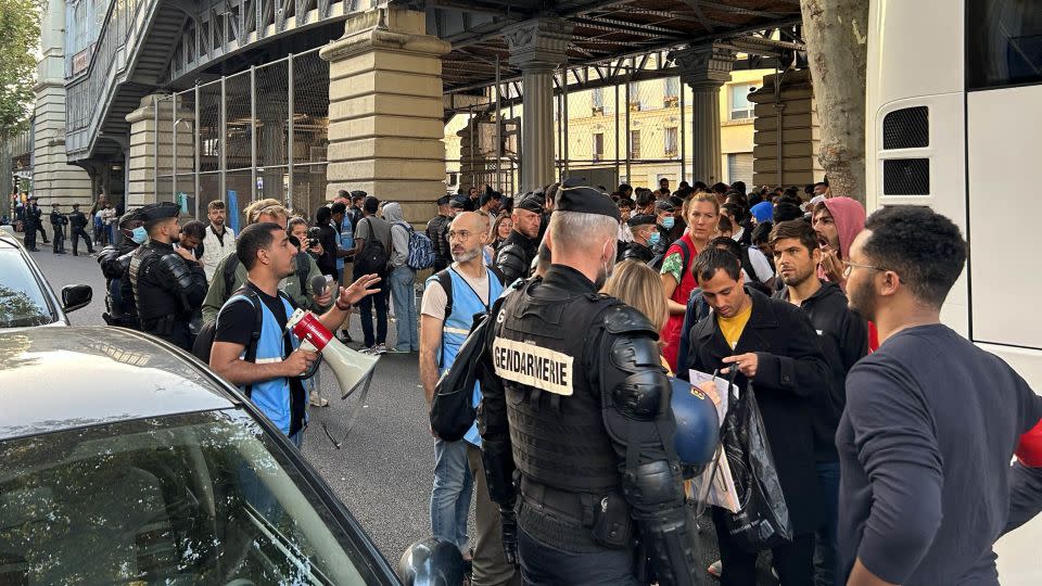 Police and workers from humanitarian organizations talk to those waiting to board a bus by the homeless camp in Paris. - Claudia Colliva/CNN