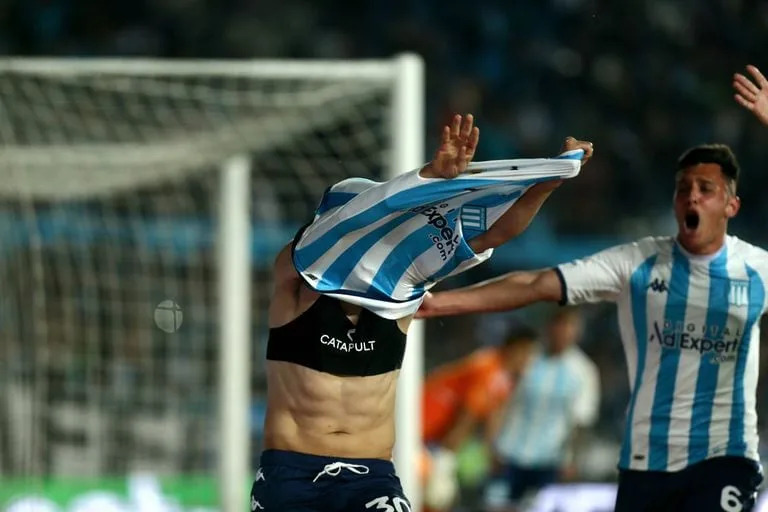 Un futbolista de Racing se quita la camiseta para celebrar un gol; debajo, el dispositivo GPS