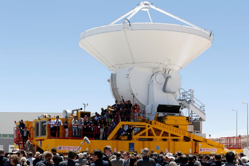 FILE PHOTO: Workers of ALMA and visitors gather around a special vehicle as it loads a parabolic antenna during the ALMA observatory inauguration near Calama