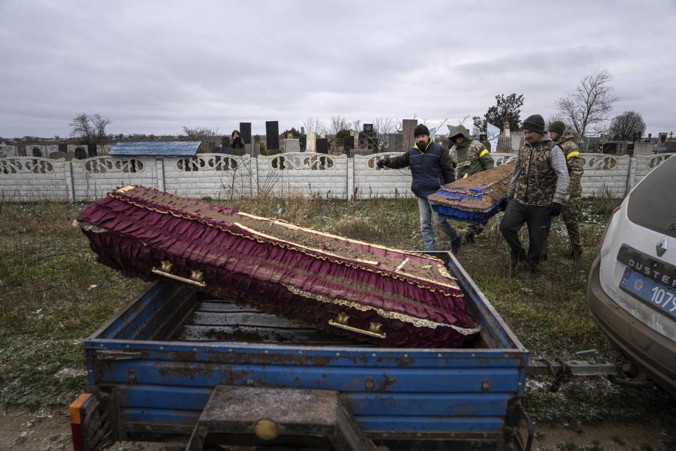 FILE - Olexandr Manzirokha, left, helps police officers to carry the coffin of his relative Henadiy Vengrynovskyi, who was shot dead in their car by Russian forces during exhumation at the cemetery in recently liberated village of Tavriiske, Kherson region, Ukraine, Tuesday, Dec. 6, 2022. Since October, Moscow has particularly focused on pummeling energy facilities and other key infrastructure with missile and drone strikes in an apparent hope of breaking the will of the Ukrainians and forcing Kyiv to negotiate on Russia's terms. (AP Photo/Evgeniy Maloletka, File)