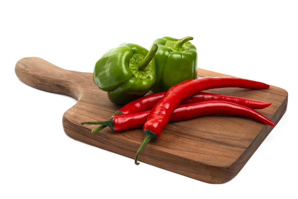 Wooden board of green bell and red chili peppers isolated on white background. High quality photo