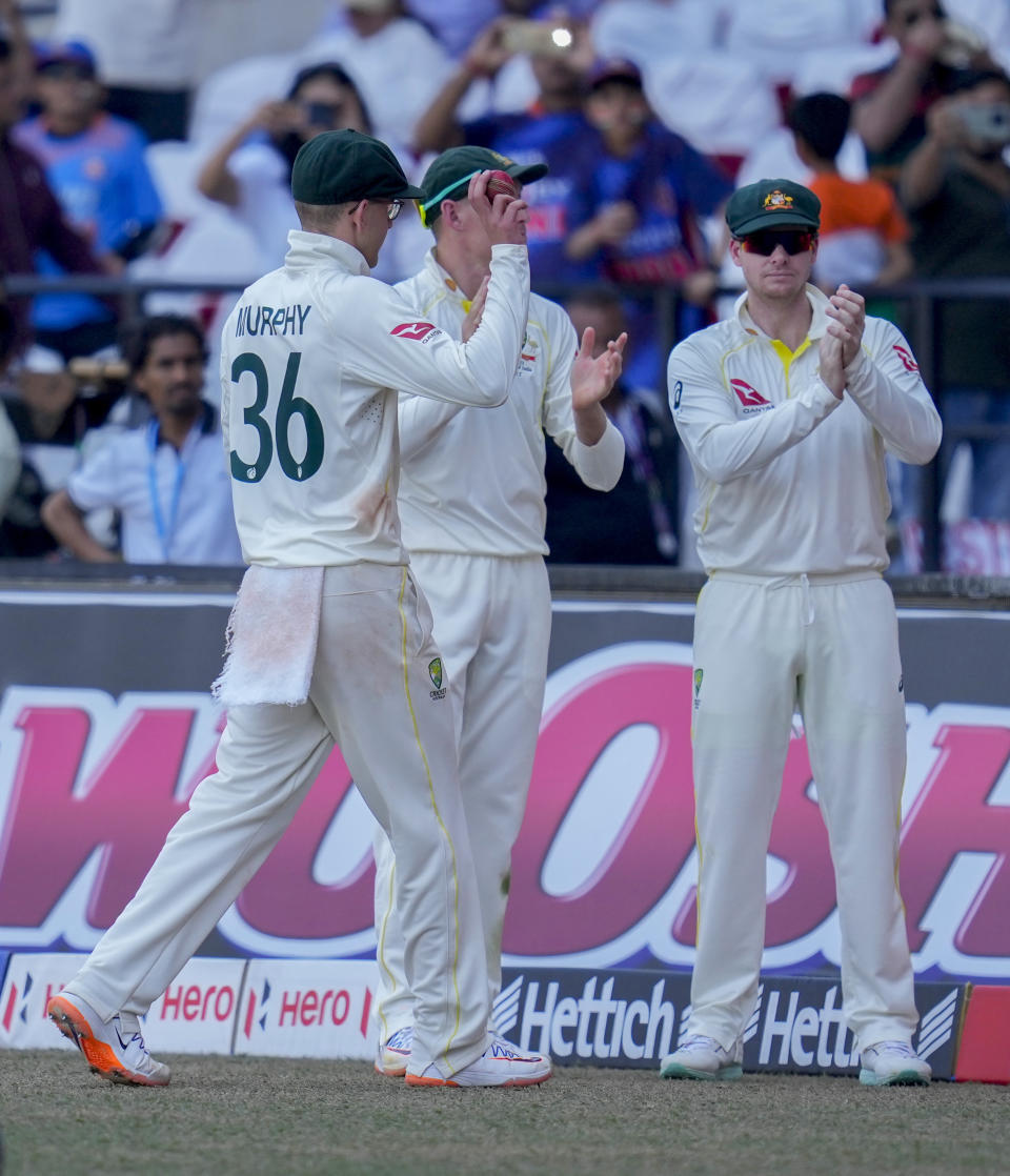 Australia's Todd Murphy, left, displays the ball after taking seven wickets as he walks back pavilion for lunch break during the third day of the first cricket test match between India and Australia in Nagpur, India, Saturday, Feb. 11, 2023. (AP Photo/Rafiq Maqbool)