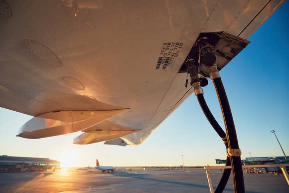 An airplane being refueled while the sun sets in the background.