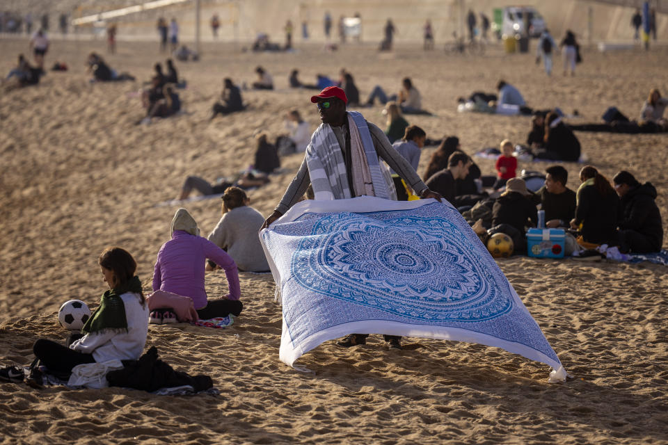 A street vendor displays sheets for sale while people sunbathe on the beach in Barcelona, Spain, Friday, Jan. 26, 2024. Spain's weather agency says recent abnormally high temperatures for this time of year are set to continue in many parts of Spain on Friday and over the weekend, with an almost summer-like feeling in many coastal areas as people take to the beaches to sunbathe and some to have a winter swim(AP Photo/Emilio Morenatti)