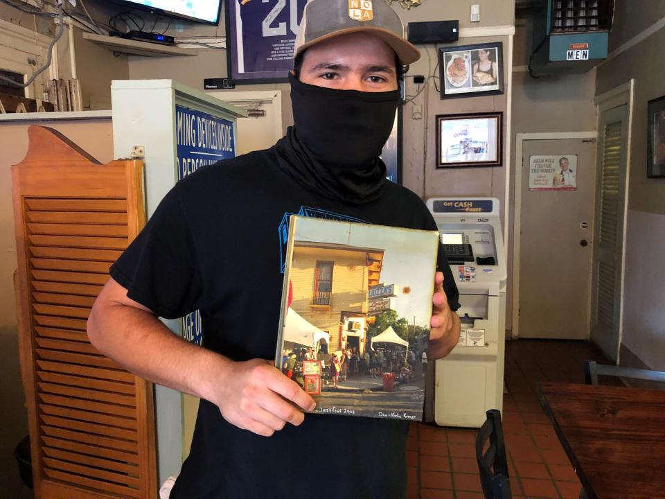 David Gonczi, a co-owner of Liuzza’s by the Track, on Wednesday, Aug. 11, 2021, holds a picture showing crowds outside the bar and restaurant during a past New Orleans Jazz and Heritage Festival. The bar and restaurant is near the site of the annual festival at the Fair Grounds Race Course. Owners and workers at the business say tourists make up a large share of their business at Jazz Fest time. But the festival was canceled in 2020 due to the COVID-19 pandemic. It was postponed this year, then canceled again this month, as area hospital populations swell with new patients in a surge fueled by the delta variant of the virus and the state’s low vaccination rate. (AP Photo/Kevin McGill)