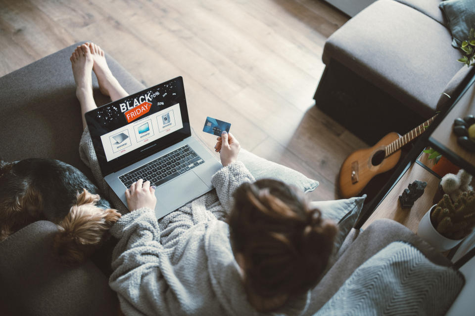 Person shopping online for Black Friday deals with a laptop and credit card, while a small dog sleeps beside them on a couch; a guitar rests nearby