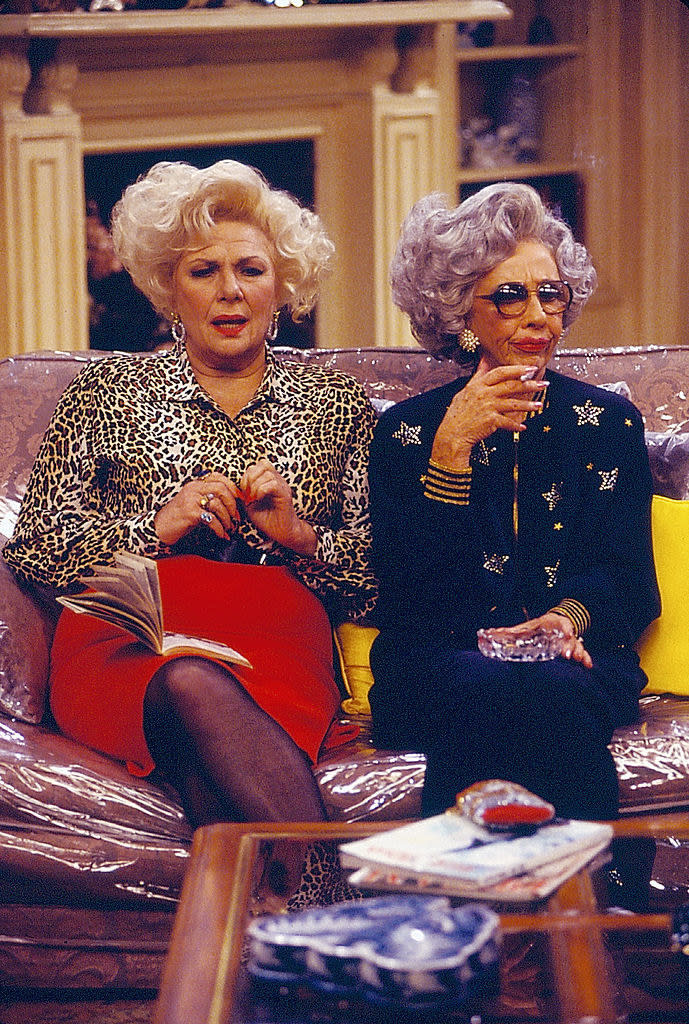 Yetta and Sylvia sitting on a couch smoking and drinking