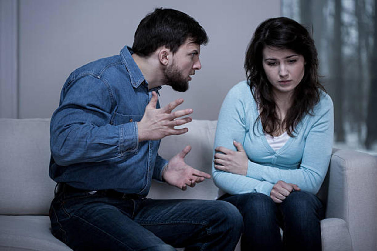 A woman sitting on the couch and a man screaming violently sitting next to her.