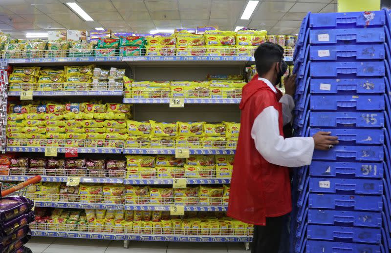 A worker pushes shopping baskets next to packets of Nestle's Maggi noodles and Reliance's Snac tac noodles inside a Reliance supermarket in Mumbai