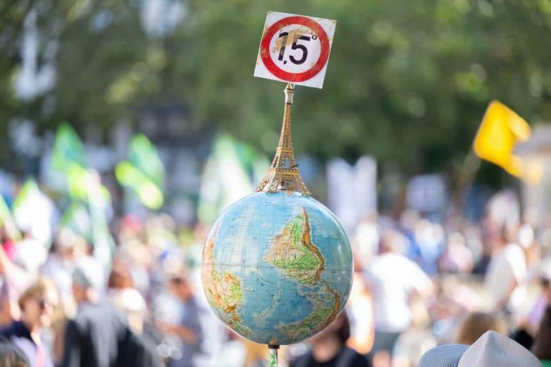 A man carries a globe with a miniature Eiffel Tower and the 1.5-degree target of the Paris climate protection agreement during a demonstration in front of the Alte Oper in Frankfurt. Germany's Fridays for Future climate protest movement is calling for demonstrations on March 31 to demand more action to address climate change. Boris Roessler/dpa