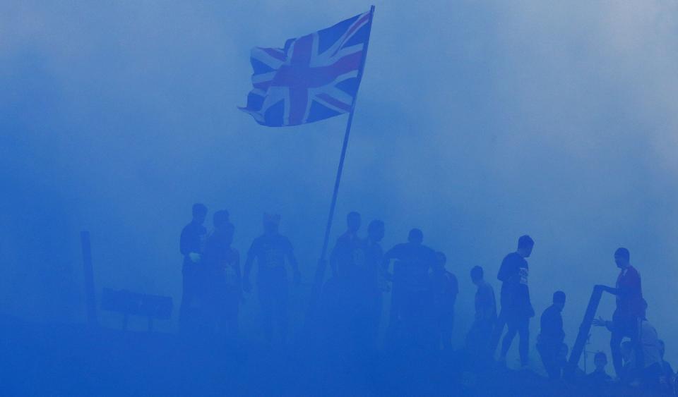 Competitors pass a Union flag as they run through clouds of blue smoke during the Tough Guy event in Perton