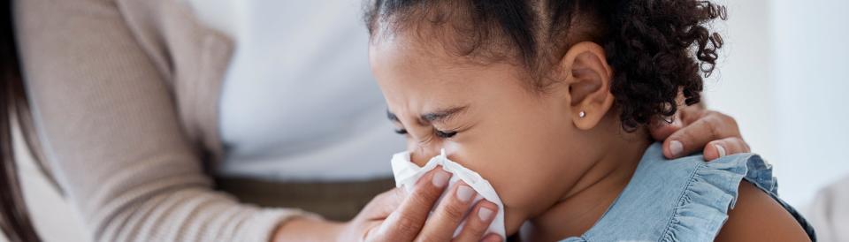 An adult helping a young girl blow her nose