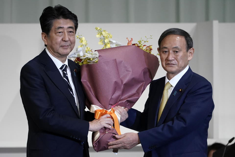 FILE - In this Sept. 14, 2020, file photo, Japan's then Prime Minister Shinzo Abe, left, receives flowers from then Chief Cabinet Secretary Yoshihide Suga after Suga was elected as new head of Japan's ruling party at the Liberal Democratic Party's (LDP) leadership election in Tokyo. Japan's new Prime Minister Suga heads to Vietnam and Indonesia on Sunday, Oct. 18, 2020, on his first overseas foray since taking over from his former boss Abe last month. (AP Photo/Eugene Hoshiko, Pool, File)