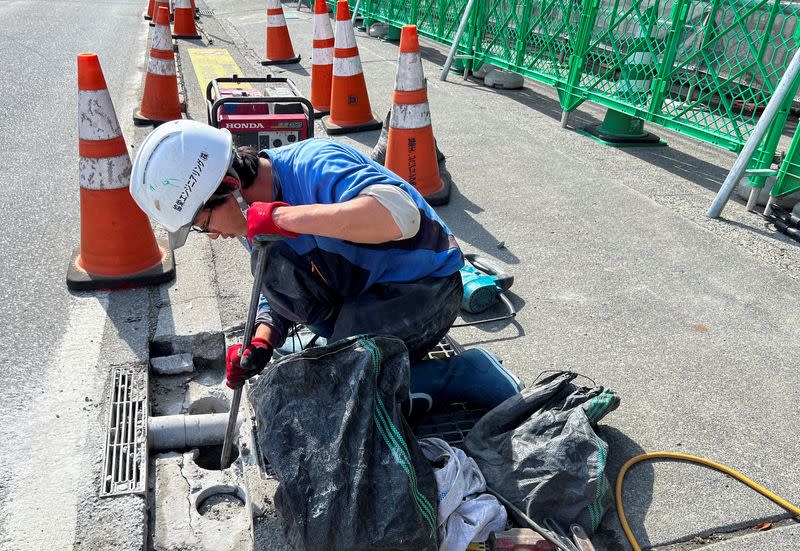 A construction worker digs a hole in the ground to build a black screen barrier near a viral photo spot for taking pictures of Mount Fuji and a convenience store, in Fujikawaguchiko