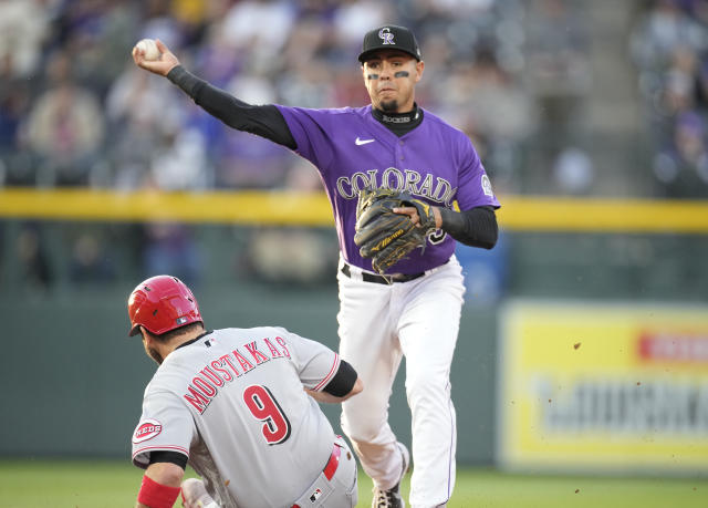 Colorado Rockies' Ryan McMahon, left, gestures to the dugout after hitting  a triple to drive in two runs as Cincinnati Reds third baseman Mike  Moustakas looks on in the sixth inning of