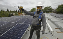 Gen Nashimoto, of Luminalt, holds a drill as he installs solar panels in Hayward, Calif., on Wednesday, April 29, 2020. From New York to California, the U.S renewable energy industry is reeling from the new coronavirus pandemic, which has delayed construction and sowed doubts about major projects on the drawing board. (AP Photo/Ben Margot)