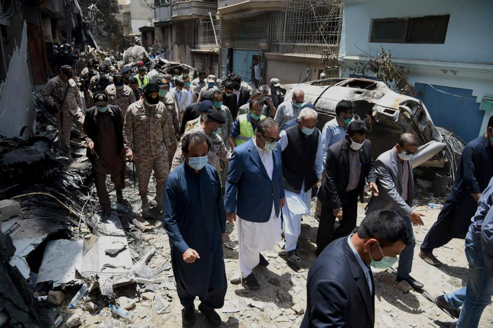 In this photo released by Pakistan Civil Aviation Authority, provincial governor Imran Ismail, center in blue coat, and Pakistan's aviation minister Ghulam Sarwar, center in black waistcoat, visit the site of Friday's plane crash, in Karachi, Pakistan, Saturday, May 23, 2020. A passenger plane belonging to state-run Pakistan International Airlines carrying passengers and crew crashed Friday near the southern port city of Karachi. (Pakistan Civil Aviation Authority via AP)