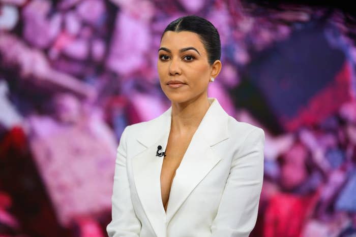 Kourtney Kardashian wearing a white blazer, posing in front of a floral backdrop