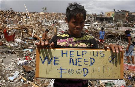 A typhoon victim holds a placard asking for food while standing amongst the ruins of houses destroyed by super typhoon Haiyan in Tanauan, Leyte in central Philippines November 14, 2013. REUTERS/Erik De Castro