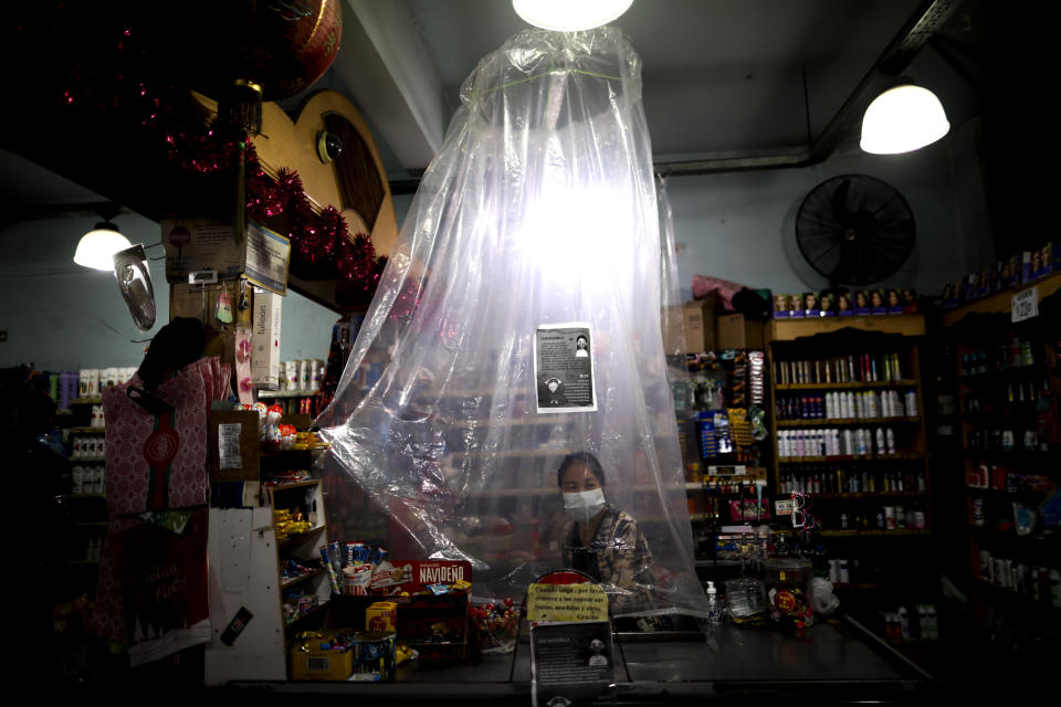 FILE - In this March 16, 2020, file photo, supermarket cashier waits for costumers behind a makeshift plastic curtain as a precaution against the spread of the new coronavirus, in Buenos Aires, Argentina. Grocery workers across the globe are working the front lines during lockdowns meant to keep the coronavirus from spreading. (AP Photo/Natacha Pisarenko)