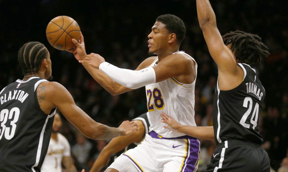 Los Angeles Lakers forward Rui Hachimura (28) passes the ball from between Brooklyn Nets center Nic Claxton (33) and guard Cam Thomas (24) during the first half of an NBA basketball game Sunday, March 31, 2024, in New York. (AP Photo/John Munson)