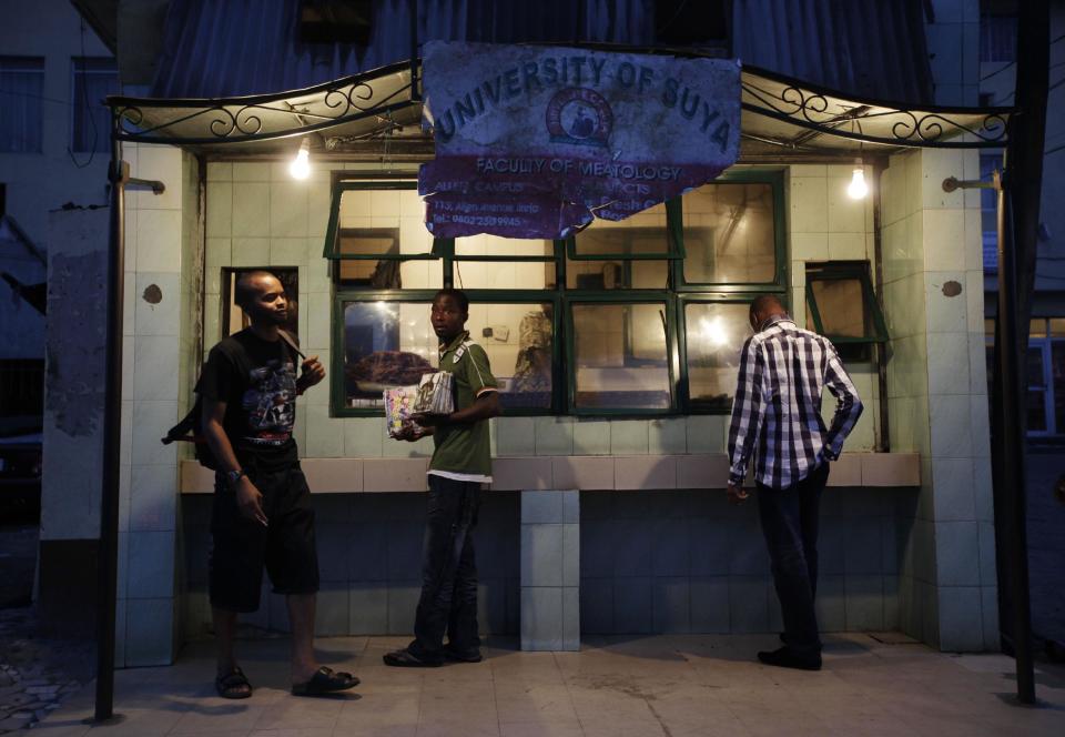 In this photo taken on Saturday, Oct. 20, 2012, customers wait to buy suya at a place called, "University of Suya," in Lagos, Nigeria. As night falls across Nigeria, men fan the flames of charcoal grills by candlelight or under naked light bulbs, the smoke rising in the air with the smell of spices and cooking meat. Despite the sometimes intense diversity of faith and ethnicity in this nation of 160 million people, that thinly sliced meat called suya, is eaten everywhere. (AP Photo/Sunday Alamba)