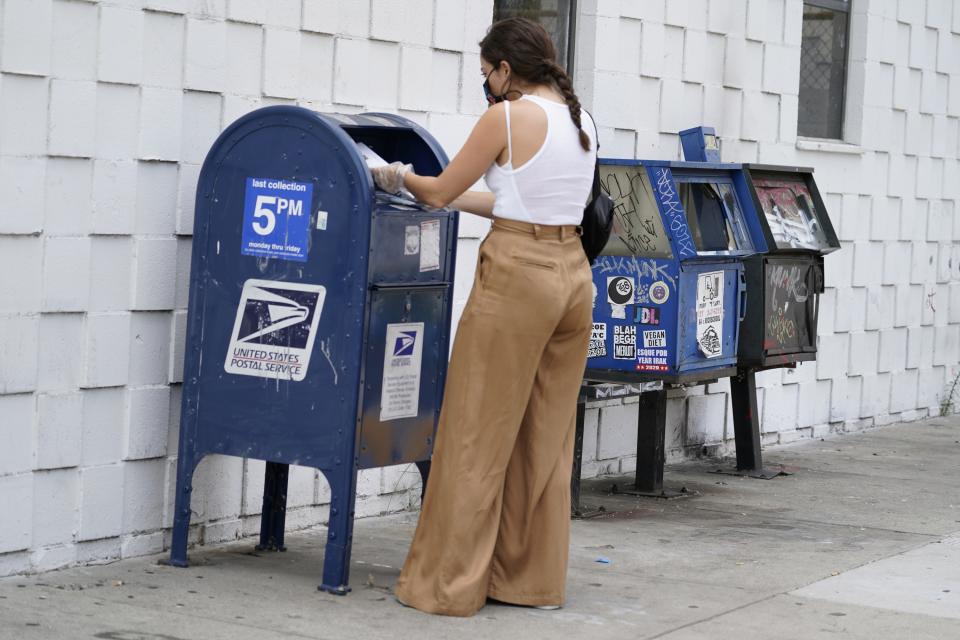 A customer wears a face mask and gloves as she drops mail into a curbside mail collection box in Los Angeles Monday, Aug. 17, 2020. (AP Photo/Damian Dovarganes)