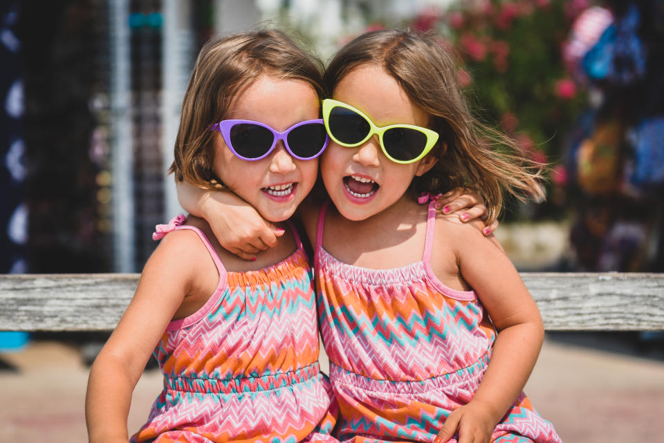 Identical twin girls on summer vacation posing for camera. Happy joyful children in the summertime with child sun glasses and pink dresses.