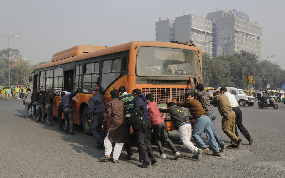 FILE- In this Jan. 1, 2016, file photo, passengers and traffic officers push a bus after it broke down in a traffic intersection on the first day of a two-week experiment to reduce the number of cars to fight pollution in New Delhi, India. India is grappling with two public health emergencies: critically polluted air and the pandemic. Nowhere is this dual threat more pronounced than in the Indian capital New Delhi, where the spike in winter pollution levels has coincided with a surge of COVID-19 cases. (AP Photo/Altaf Qadri, File)