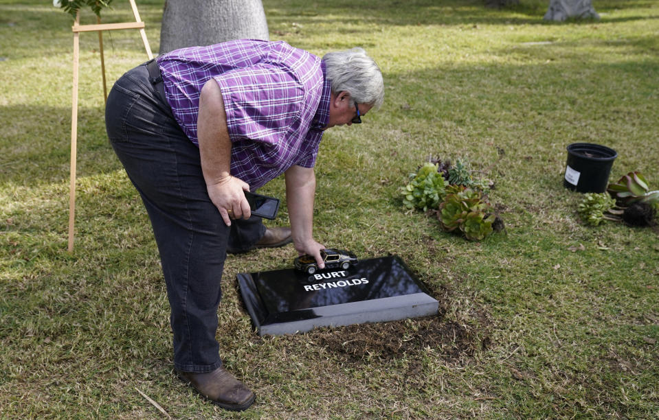 Burt Reynolds fan Dan Redmond, of Calamesa, Calif., places a model of the Trans Am from the 1977 film "Smokey and the Bandit" on a temporary headstone for the late actor at Hollywood Forever cemetery, Thursday, Feb. 11, 2021, in Los Angeles. Reynolds' cremated remains were moved from Florida to Hollywood Forever, where a small ceremony was held Thursday. A permanent gravesite will be put up for Reynolds in a few months. (AP Photo/Chris Pizzello)