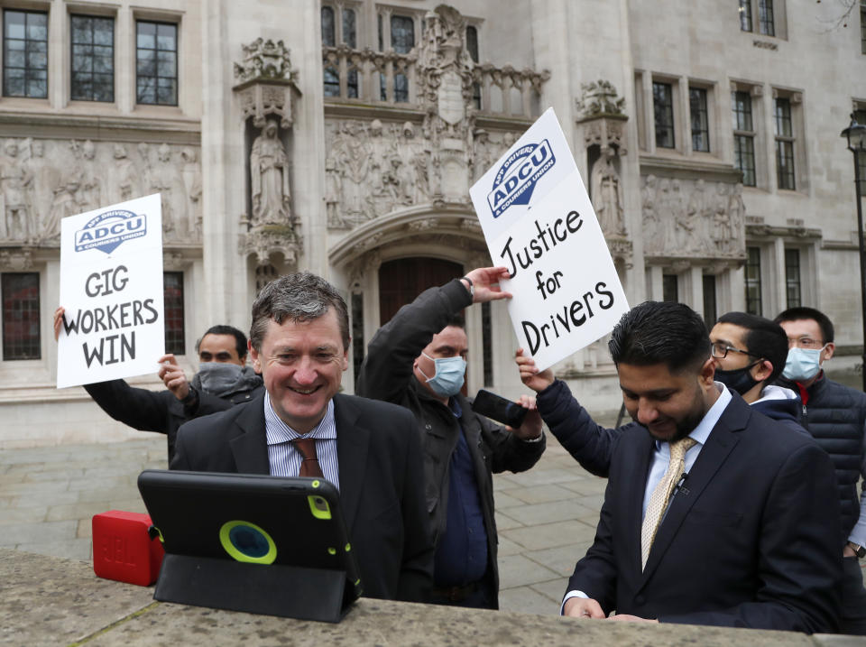 Uber drivers of the (ADCU), App Drivers & Couriers Union, celebrate as they listen to the court decision on a tablet computer outside the Supreme Court in London, Friday, Feb. 19, 2021. The U.K. Supreme Court ruled Friday that Uber drivers should be classed as “workers” and not self employed.(AP Photo/Frank Augstein)