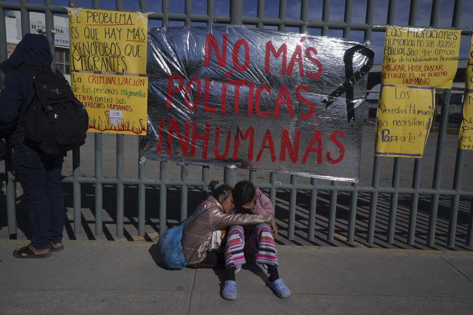 A pair of Venezuelan sisters comfort each other sitting on a sidewalk outside an immigration detention center where dozens of migrants fearing deportation set mattresses ablaze, starting a fire that killed at least 40 people, in Ciudad Juarez, Mexico, Tuesday, March 28, 2023. The sign behind the sisters reads in Spanish "No more inhuman policies." (AP Photo/Fernando Llano)