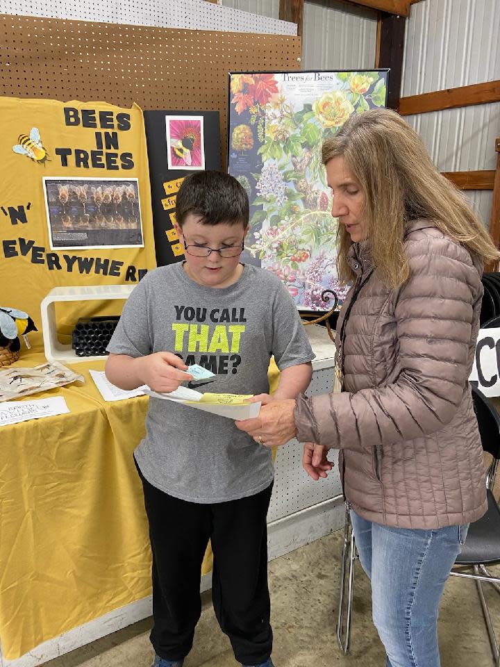 Eli Coons, a member of the Peas in a Pod junior gardeners, shares a native seed packet and honey bee information with June Rauchenstein during the plant sale that was held in May by the Earth, Wind and Flowers Garden Club.