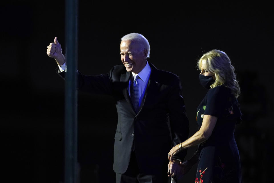 President-elect Joe Biden stands on stage with his wife Jill Biden as he gives the thumbs-up to the cheering crowd beyond the protective glass, Saturday, Nov. 7, 2020, in Wilmington, Del. (AP Photo/Carolyn Kaster)
