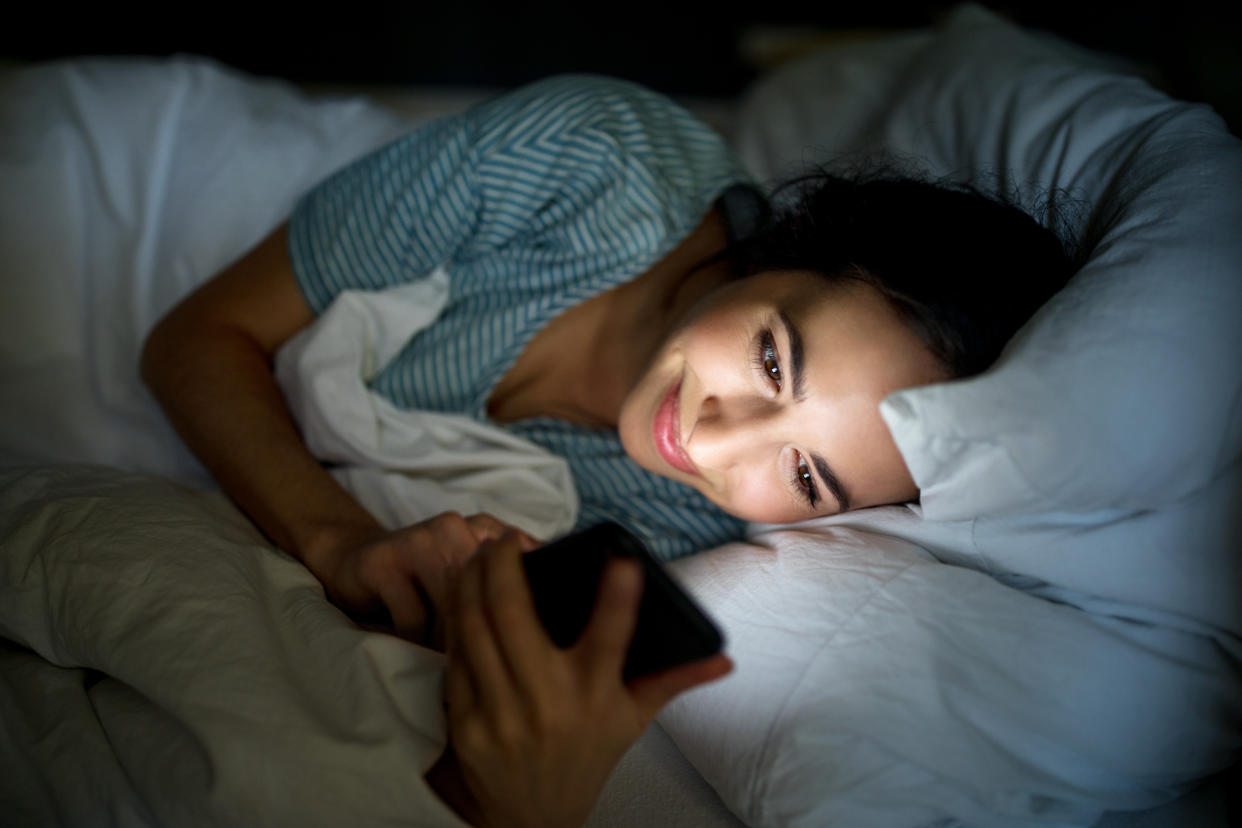 Beautiful woman checking her cell phone while lying on bed at home. Woman using mobile phone at bedtime.