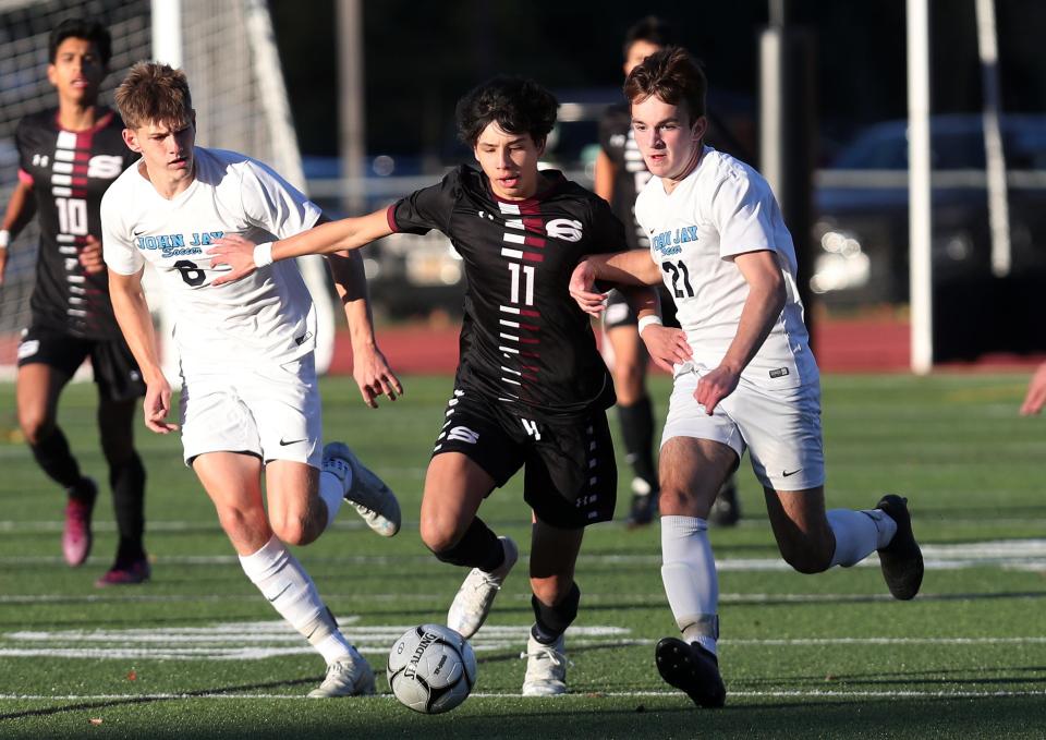 Scarsdale's Lorenzo Galeano (11) battles for ball control with John Jay's Jordan Dixon (6) and Derek Viebrock (21) during boys soccer playoff action at Scarsdale High School Oct. 27, 2022.