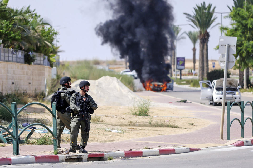 Israeli soldiers take position in the southern Israeli town of Ofakim on Sunday, Oct. 8, 2023. Hamas militants stormed over the border fence Saturday, killing hundreds of Israelis in surrounding communities. The burning car was used by the gunmen and set on fire by the residents.  (Ilan Assayag / AP)