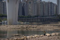 A man wipes his forehead as he walks along the lower than normal bank of the Jialing River in southwestern China's Chongqing Municipality, Friday, Aug. 19, 2022. Ships crept down the middle of the Yangtze on Friday after the driest summer in six decades left one of the mightiest rivers shrunk to barely half its normal width and set off a scramble to contain damage to a weak economy in a politically sensitive year. (AP Photo/Mark Schiefelbein)